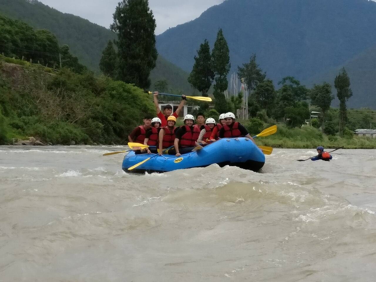 Rafters paddling a blue raft through white water in Punakha